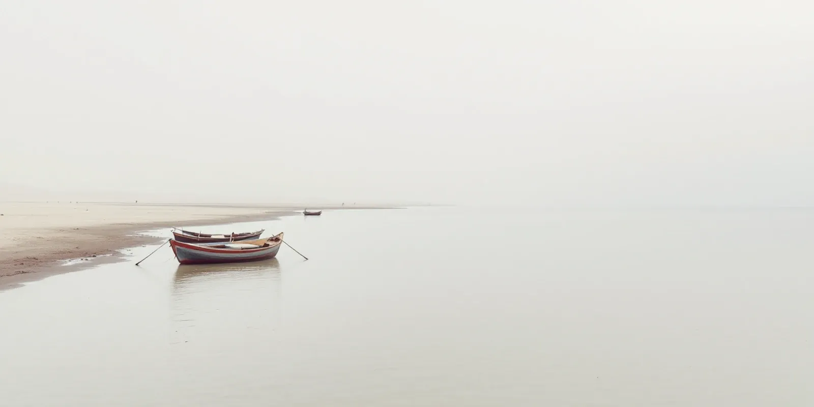 Barcas de pesca de madera en la orilla de una laguna en calma, con la costa llana perdiéndose en la bruma