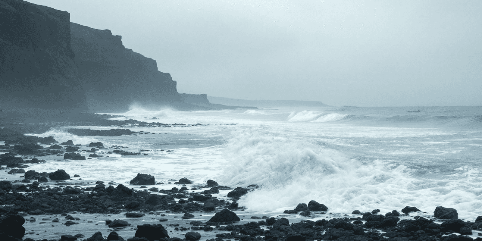 Oleaje del Atlántico rompiendo contra una costa de roca volcánica negra bajo un cielo gris