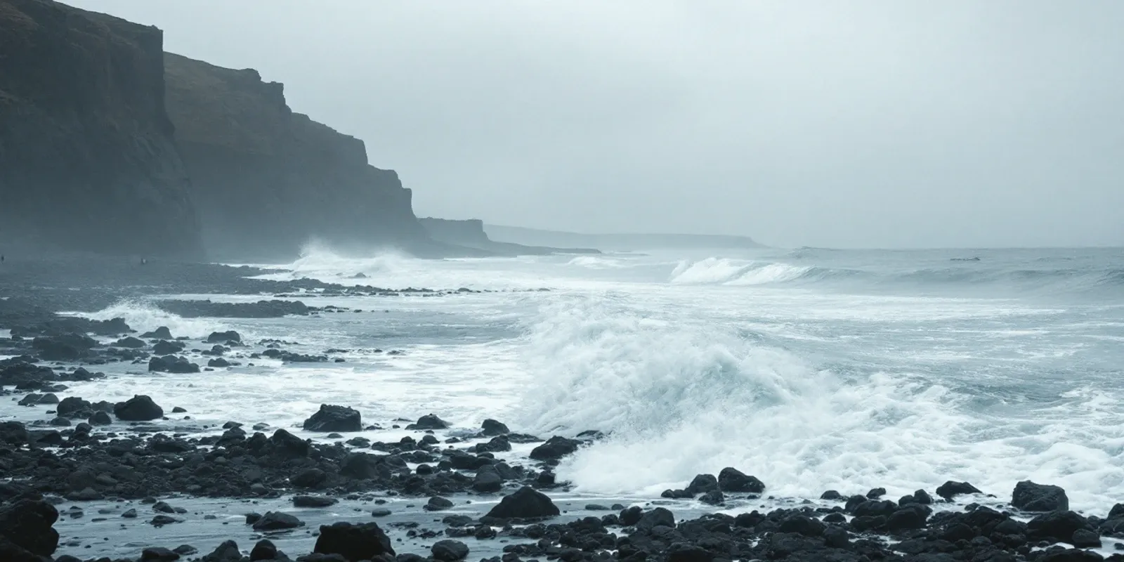 Oleaje del Atlántico rompiendo contra una costa de roca volcánica negra bajo un cielo gris