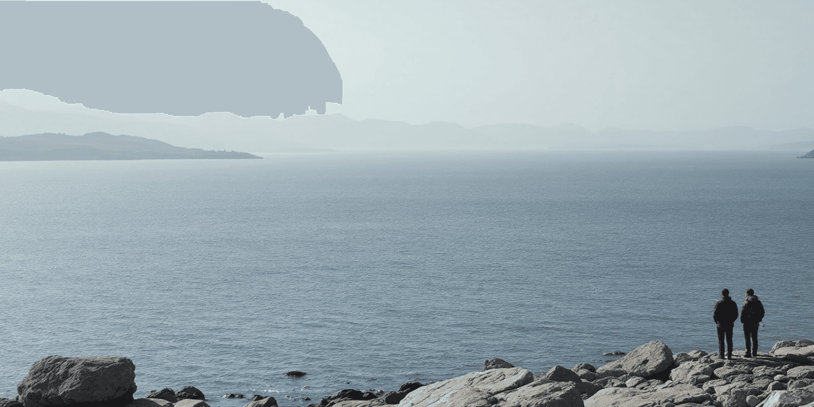 Estrecho gris azulado visto desde una orilla rocosa, con la costa de enfrente en el horizonte
